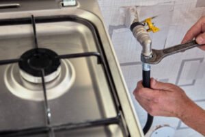 A man repairs a gas stove using a wrench, focused on fixing the appliance in a well-lit kitchen.