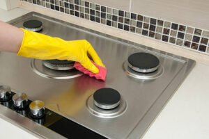 A person in yellow gloves scrubbing a stove top, focused on cleaning the surface thoroughly.
