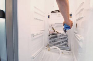 A person inspects a refrigerator during refrigeration repair, opening the door to check its contents inside.